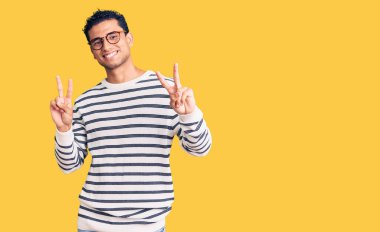 Sıradan kıyafetler ve gözlük takmış İspanyol yakışıklı genç adam kameraya bakıp zafer işareti yapıyor. İki numara.. 