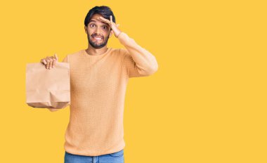 Elinde paket kâğıt torbası tutan yakışıklı İspanyol bir adam. Kafası karışık, şaşırmış ve sinirli bir yüzü var. 