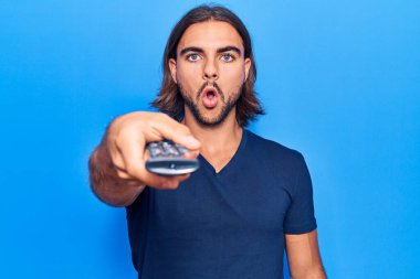 Televizyonun uzaktan kumandasını tutan yakışıklı genç adam korkmuş ve ağzı açık kalmış, şaşırmış ve şaşırmış. 