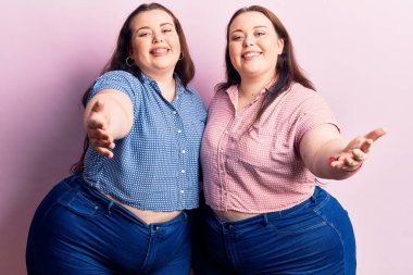 Genç ve cüsseli ikizler sıradan kıyafetler giyip kameraya bakıyor ve kucaklaşmak için kollarını açıp gülümsüyor. Mutluluğu kucaklayan neşeli bir ifade.. 