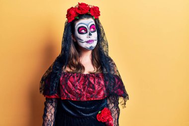 Sarı üzerine ölü kostümü giymiş genç bir kadın. Gülümsüyor, yan tarafa bakıyor ve düşünüyor.. 