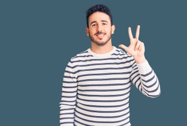 Gündelik kıyafetler giyen genç İspanyol adam üç numarayı gösterip işaret ederken kendinden emin ve mutlu gülümsüyor.. 