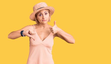 Sarışın, yaz şapkası takan genç bir kadın. Baş parmaklarını yukarı aşağı hareket ettiriyor. Anlaşmazlık ve uzlaşma ifadesi. çılgın çatışma 