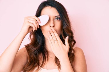 Genç, güzel esmer kadın elinde makyaj süngeri tutarak ağzını eliyle kapatmış, şok olmuş ve hata yapmaktan korkan. şaşırmış ifade 