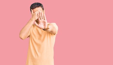 Ayılı yakışıklı genç adam gündelik sarı tişörtler giyiyor gözleri ellerle örtüyor ve üzgün ve korku ifadeleriyle jest yapıyor. utangaç ve olumsuz kavram. 