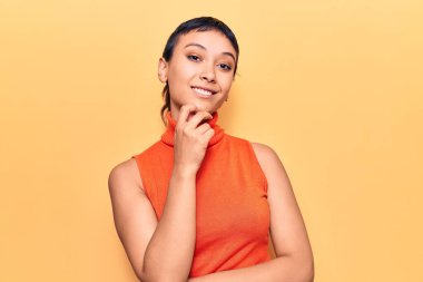 Gündelik giysiler giyen genç bir kadın kameraya kollarını kavuşturmuş ve çenesi üzerinde kendinden emin bir şekilde gülümsüyor. Olumlu düşünmek. 