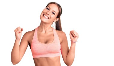 Spor kıyafetleri giyen genç ve güzel bir İspanyol kadın kollarını kaldırıp gözleri açık bir şekilde başarıyı kutluyor ve şaşırıyor. Kazanan konsept. 