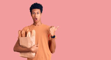 Genç Afro-Amerikalı bir adam elinde kağıt torbayla elini kaldırdığında şaşırmış ve ağzı açık bir şekilde hayrete düşmüş.. 