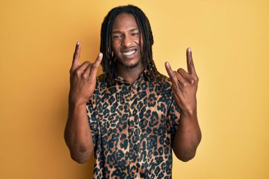 Saçları örgülü, leopar desenli hayvan desenli tişörtlü çılgın bir ifadeyle bağıran, elleri havada rock sembolü yapan Afrikalı Amerikalı bir adam. Müzik yıldızı. ağır kavram. 