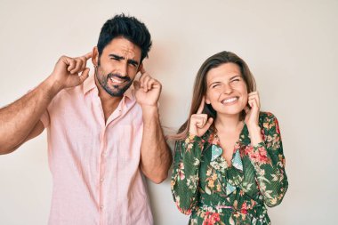 Beautiful young couple of boyfriend and girlfriend together covering ears with fingers with annoyed expression for the noise of loud music. deaf concept.  clipart