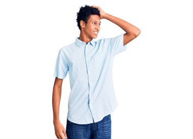 Genç Afro-Amerikalı, günlük kıyafetler giymiş, gülümseyen, kendine güvenen, el hareketleriyle saçlara dokunan, çekici ve modaya uygun poz veren bir adam. 