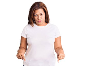 Orta yaşlı, beyaz tişörtlü bir kadın üzgün ve üzgün görünüyor, parmaklarıyla yönü gösteriyor, mutsuz ve depresif.. 