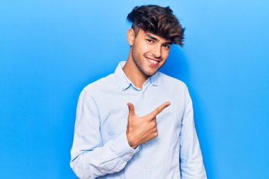 Gündelik giysiler giyen genç İspanyol adam gülümseyen, eli ve parmağı yana doğru gösteren. 