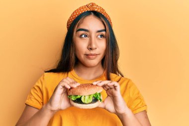 Lezzetli bir klasik burger yiyen genç Latin kadın gülümseyip yan tarafa bakıyor ve düşünüyor.. 