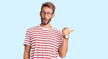 Sakallı, sıradan giyinen ve gözlüklü yakışıklı sarışın adam el parmağı yana dönük, ağzı açık, şaşkın bir ifade sergiliyor.. 