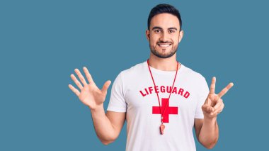 Cankurtaran üniforması giyen genç yakışıklı adam yedinci parmaklarını gösterip işaret ederken kendinden emin ve mutlu gülümsüyor.. 