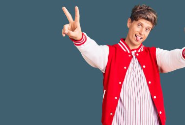 Beyzbol üniforması giyen yakışıklı genç adam iki elini de göstererek gülümsüyor ve zafer işareti yapıyor. İki numara.. 