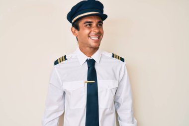 Uçak pilotu üniforması giyen genç İspanyol adam yüzünde gülümsemeyle yan yana bakıyor, doğal bir ifade. Kendinden emin gülen. 