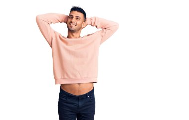 Genç İspanyol bir adam günlük kıyafetler giyiyor rahatlıyor ve esniyor, kolları ve elleri başının arkasında mutlu bir şekilde gülümsüyor. 