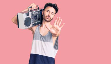 Kasetçalar tutan genç İspanyol adam, açık elle müzik dinliyor dur işareti yapıyor ciddi ve kendinden emin bir ifadeyle, savunma jesti 