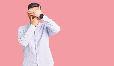 Zarif iş gömleği ve gözlük takan yakışıklı genç adam gözlerini ve ağzını elleriyle kapatıyor, şaşırmış ve şok olmuş. duygu gizleme 