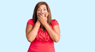 Orta yaşlı, gündelik giysiler giyen Latin bir kadın yanlışlıkla elleriyle ağzını kapatırken şok oldu. gizli kavram. 