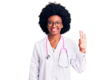 Genç Afro-Amerikalı kadın doktor önlüğü ve steteskop giyip üç numarayı gösterirken kendinden emin ve mutlu bir şekilde gülümsüyor.. 