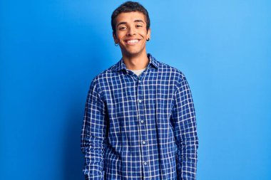 Genç Afro-Amerikalı sıradan kıyafetler giyen bir adam yüzünde gülümseme, doğal bir ifade ile yan yana bakıyor. Kendinden emin gülen. 