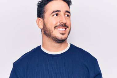 Latin kökenli genç bir adam günlük giysiler giyiyor, rahat bir görünüm takınıyor, doğal bir yüz ifadesi ve kendinden emin bir gülümsemeyle poz veriyor.. 