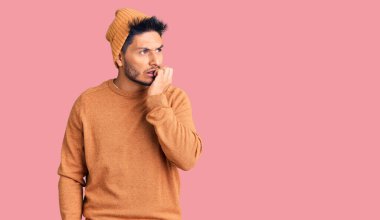 Kış süveteri ve yün şapka giyen yakışıklı Latin Amerikalı genç adam gergin ve elleri ağızdan tırnak yerken gergin görünüyor. anksiyete. 