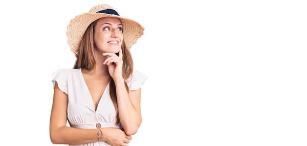 若い美しいブロンドの女性は 夏のドレスと帽子を手であごの質問について考えると 集中的な表現を身に着けている 思慮深い顔で笑顔 疑わしい概念 — ストック写真