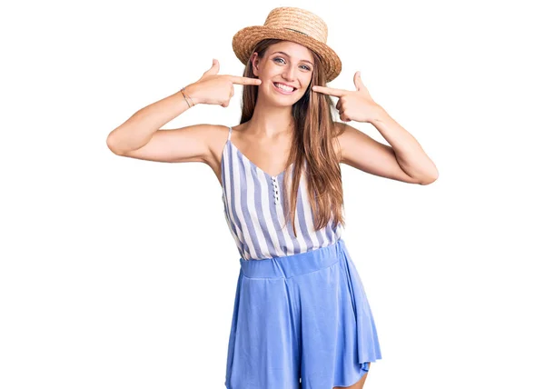 若い美しいブロンドの女性は 夏の帽子を身に着けている笑顔明るく見せ 指の歯と口で指しています 歯の健康の概念 — ストック写真
