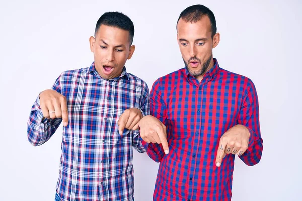 Genç eşcinsel iki adam, günlük kıyafetler giyip parmaklarını göstererek reklamlarını gösteriyorlar, şaşırmış yüzler ve açık ağızlar. 