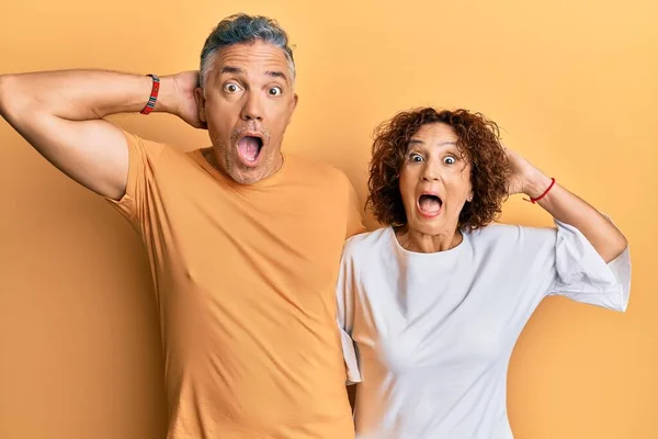 Beautiful middle age couple together wearing casual clothes crazy and scared with hands on head, afraid and surprised of shock with open mouth