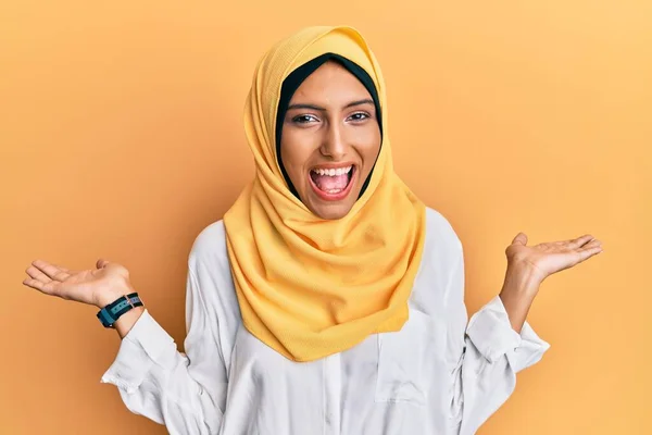 伝統的なイスラムのヒジャーブスカーフを身に着けている若いブルネットのアラブ女性は狂気を祝い 腕を上げ 興奮して叫んで目を開けて成功に驚いています 勝者のコンセプト — ストック写真
