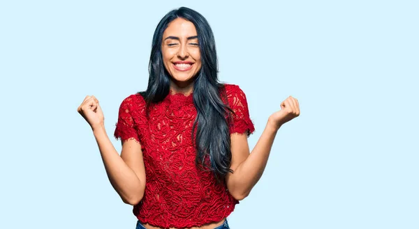 Beautiful hispanic woman wearing elegant shirt very happy and excited doing winner gesture with arms raised, smiling and screaming for success. celebration concept.