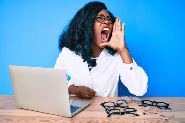 Beautiful african woman at the oculist clinic shouting and screaming loud to side with hand on mouth. communication concept.