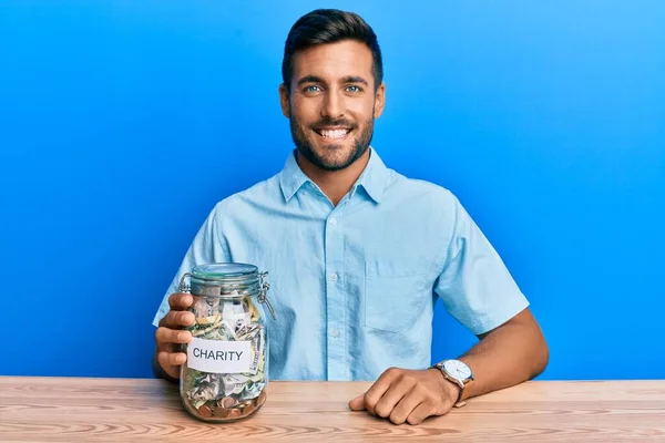 Hombre Hispano Guapo Sosteniendo Tarro Caridad Con Dinero Mirando Positivo —  Fotos de Stock