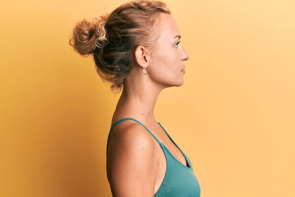 Beautiful caucasian woman wearing sleeveless shirt over yellow background looking to side, relax profile pose with natural face with confident smile. 