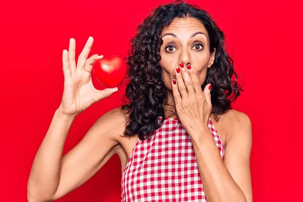 Orta yaşlı, kalbi elinde tutan güzel bir kadın. Ağzını eliyle kapatıyor. Şok geçiriyor ve hata yapmaktan korkuyor. şaşırmış ifade 