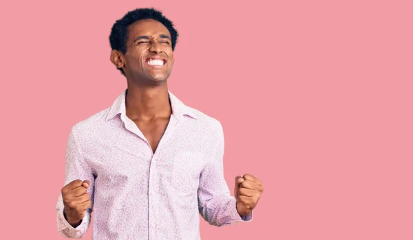 身穿休闲粉色衬衫的非洲帅哥兴奋地期待着胜利 举起双臂 闭上双眼 微笑着庆祝胜利 获奖者概念 — 图库照片