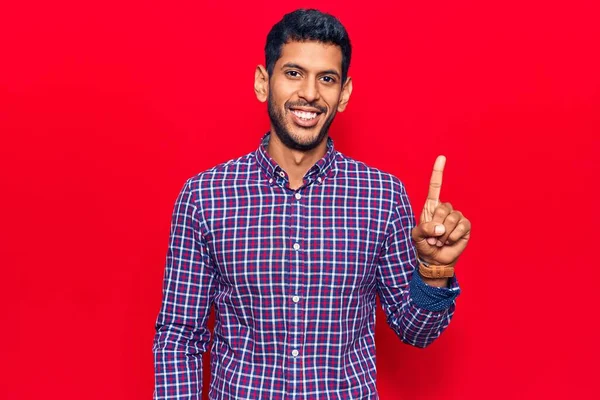 Gündelik kıyafetler giyen genç Latin bir adam bir fikir ya da soruyla gülümsüyor ve mutlu bir yüzle işaret ediyor. 