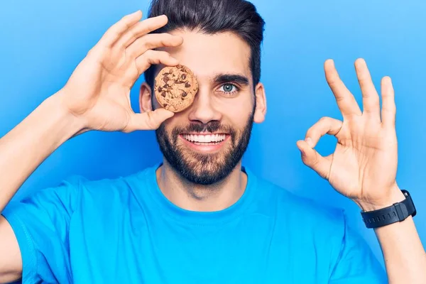 Çikolatalı kurabiye tutan genç yakışıklı adam parmaklarıyla imza atıyor, gülümseyerek mükemmel bir sembol oluşturuyor. 