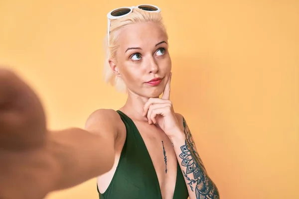 Mladá Blondýna Tetováním Plavkách Selfie Vážnou Tváří Přemýšlející Otázce Rukou — Stock fotografie