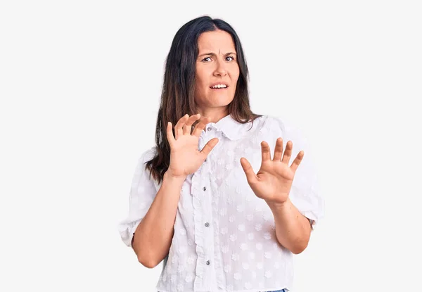 Young beautiful brunette woman wearing casual shirt disgusted expression, displeased and fearful doing disgust face because aversion reaction. with hands raised