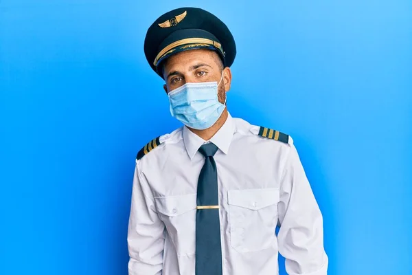 機内パイロットの制服を着た髭を生やしたハンサムな男が真剣な表情で安全マスクを着用している カメラを見ているだけで — ストック写真