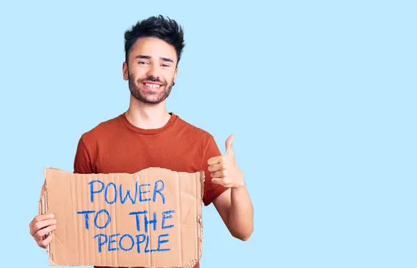 Young hispanic man holding power to the people banner smiling happy and positive, thumb up doing excellent and approval sign