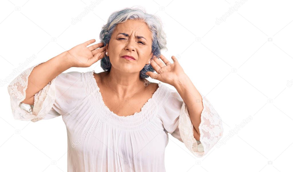 Senior woman with gray hair wearing bohemian style trying to hear both hands on ear gesture, curious for gossip. hearing problem, deaf 