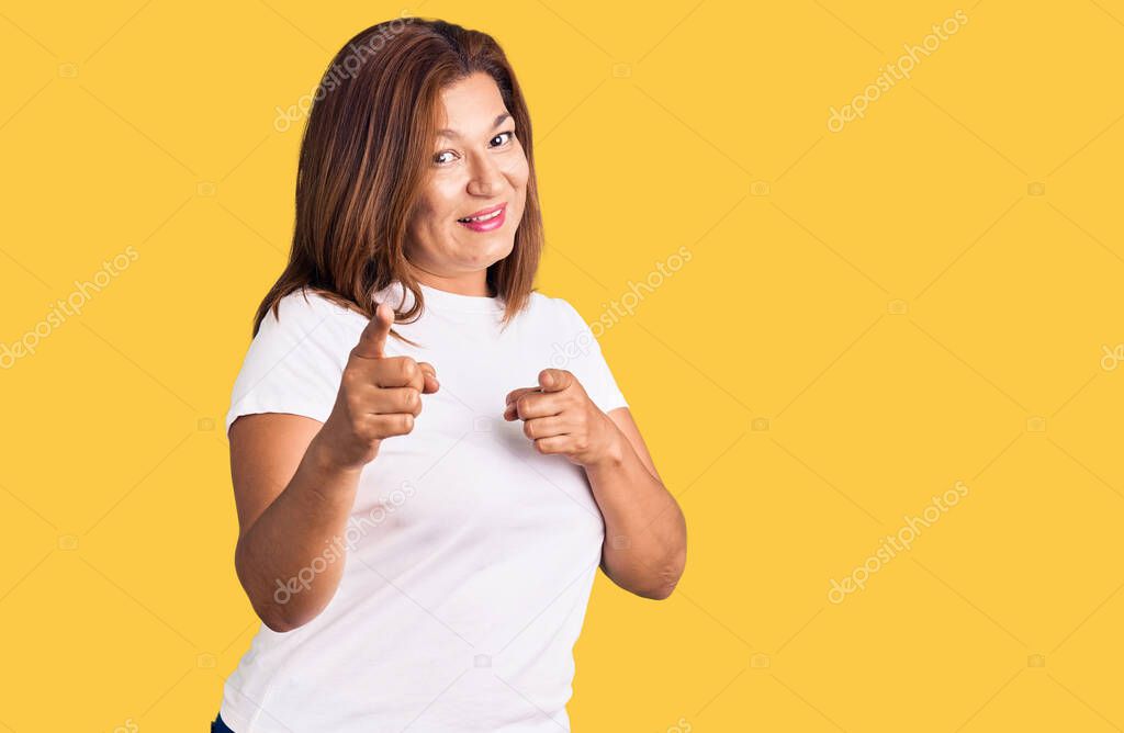 Middle age latin woman wearing casual white tshirt pointing fingers to camera with happy and funny face. good energy and vibes. 