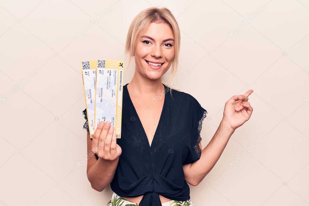 Beautiful blonde tourist woman on vacation holding airline boarding pass over white background smiling happy pointing with hand and finger to the side